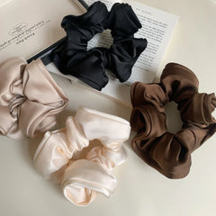 group of scrunchies in brown, black, beige, and cream placed on a book