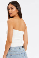 Rear view of a woman wearing a white strapless knit top with a ribbed texture, paired with light wash jeans.