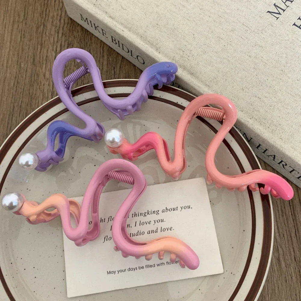 Assortment of pink, orange, and purple S-shaped hair claw clips with pearls on a saucer and book