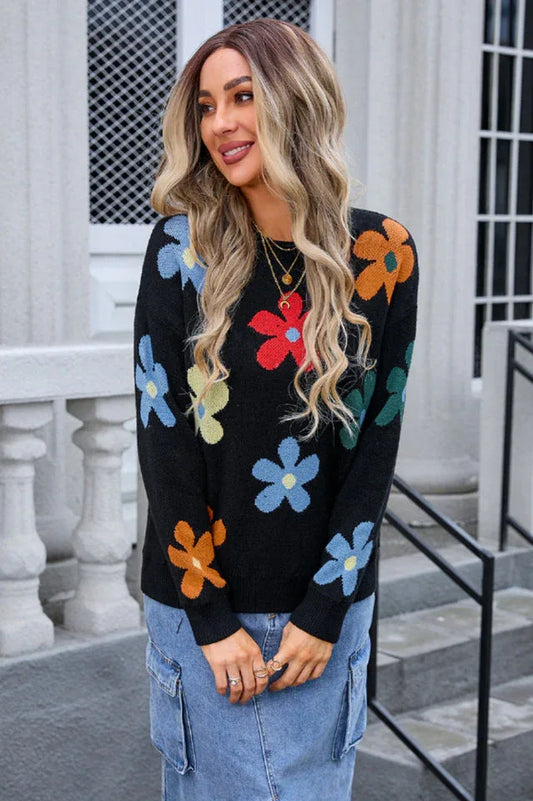 Woman wearing a black long-sleeve sweater with a colorful floral print, paired with a denim skirt.