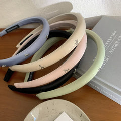 Assortment of padded headbands in various colors arranged on a wooden surface with books and a decorative plate