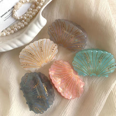 Collection of seashell hair claws in various pastel colors with gold and rhinestone embellishments