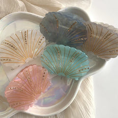 Assorted seashell hair clips arranged on a white iridescent dish