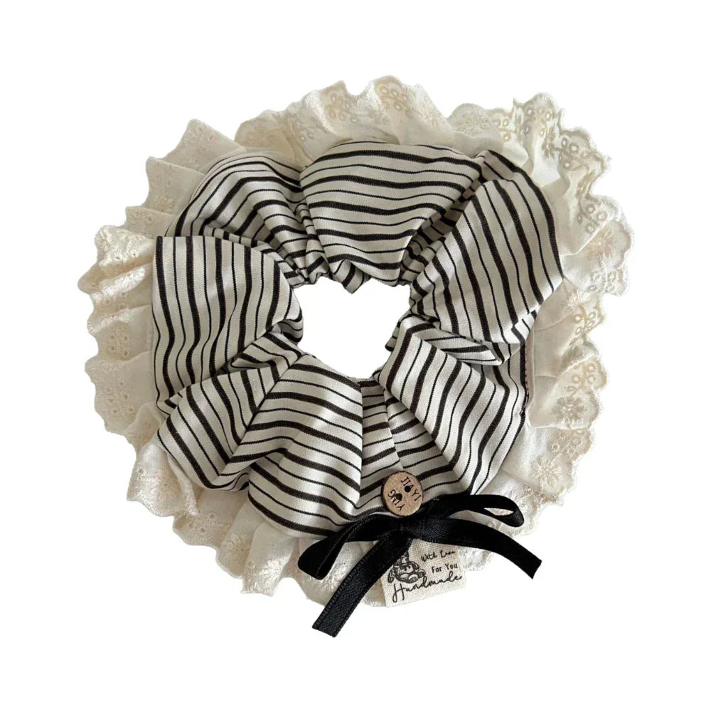 A close-up view of a black and white striped scrunchie with a lace trim and black bow.