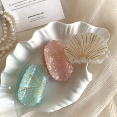 Pastel seashell hair clips displayed on a white seashell-shaped dish