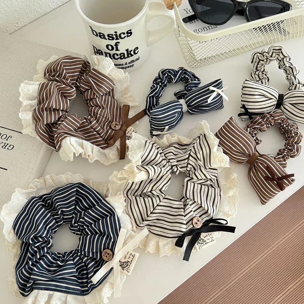 A collection of striped scrunchies with lace trim and bow accents arranged on a white surface.