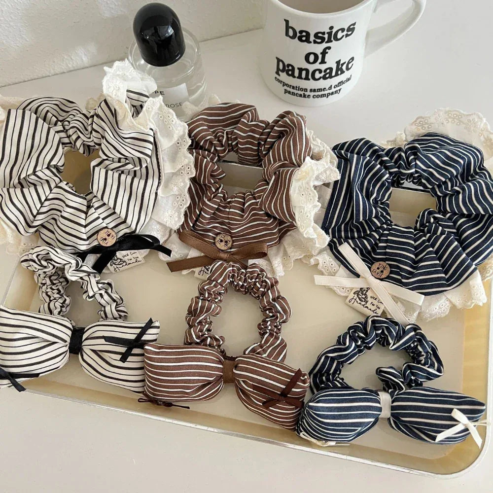 A top-down view of a collection of striped scrunchies with lace trim and bow accents, arranged on a tray.