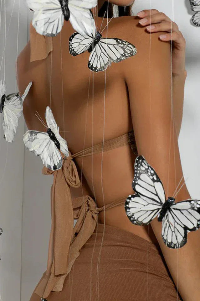Rear view of a woman wearing a gold halter top tied with a bow, with decorative butterflies attached to strings.
