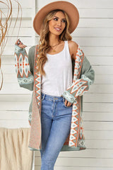 Woman wearing a long green open-front cardigan with geometric print details, a white tank top, and blue jeans.