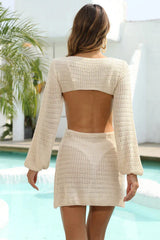 Back view of a woman wearing a cream crocheted knit mini dress with long sleeves and an open back.