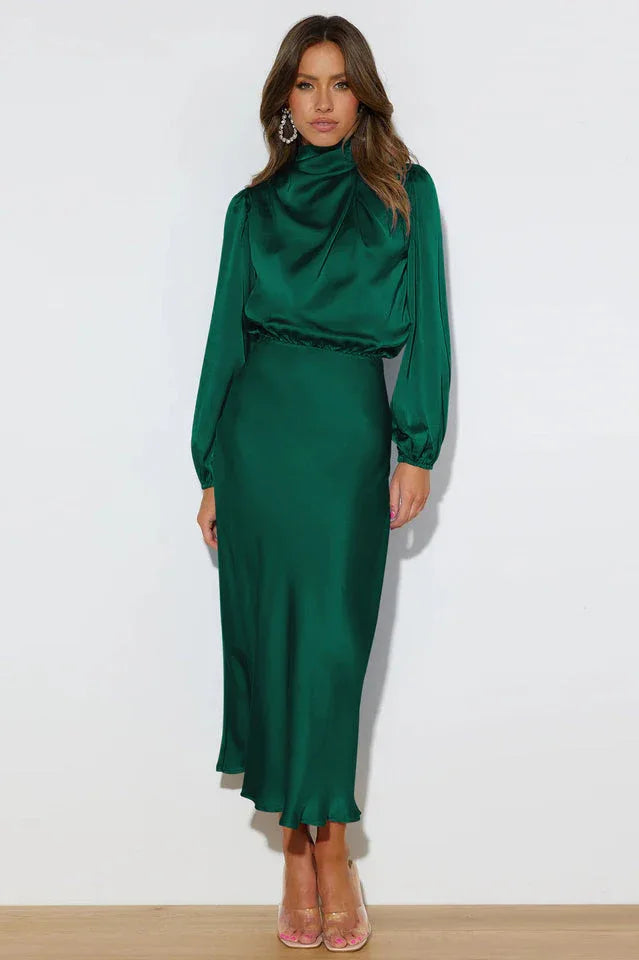 Full-length front view of a woman in an emerald green satin dress with a cowl neckline and long puff sleeves.