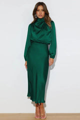 Full-length front view of a woman in an emerald green satin dress with a cowl neckline and long puff sleeves.