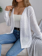 Woman in a white open-knit cardigan, white tank top, and blue jeans, seated on a couch.