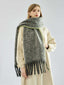 Woman wearing a long, grey, textured knit scarf with fringe detail and lime green trim, draped over a cream coat.