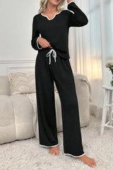 woman wearing black long sleeve pajama set with white piping, standing in a bedroom