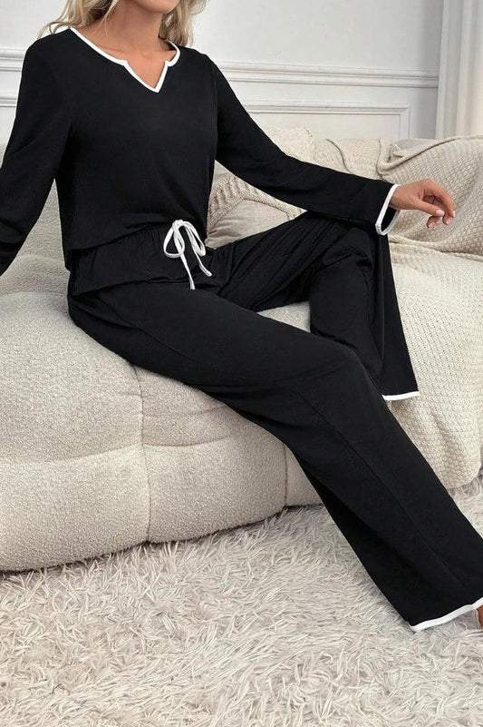 woman wearing black long sleeve pajama set with white piping, sitting on a couch