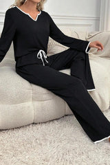 woman wearing black long sleeve pajama set with white piping, sitting on a couch