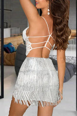 Woman wearing a white lace crop top with spaghetti straps and a strappy back, paired with a silver sequined fringe skirt, shown from the back.