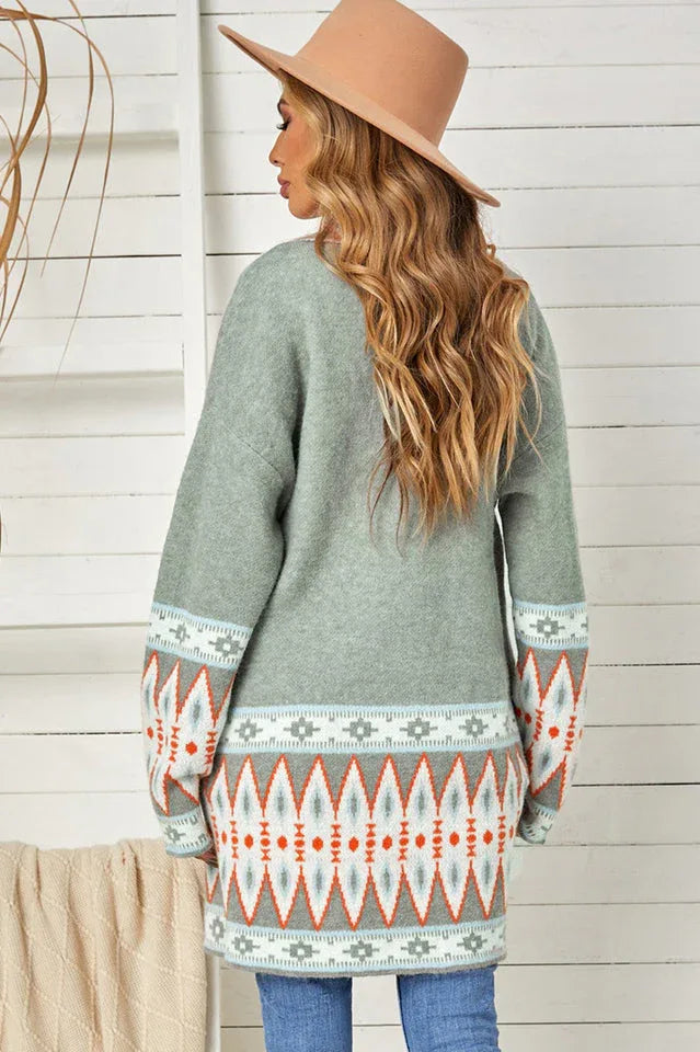 Back view of a woman wearing a long green open-front cardigan with geometric print details on the sleeves and hem.