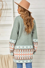 Back view of a woman wearing a long green open-front cardigan with geometric print details on the sleeves and hem.