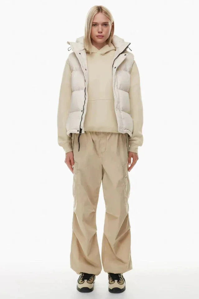 Full body shot of a woman in a cream puffer vest, cream hoodie, and tan cargo pants