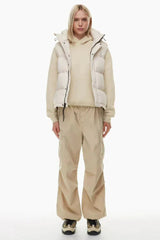 Full body shot of a woman in a cream puffer vest, cream hoodie, and tan cargo pants