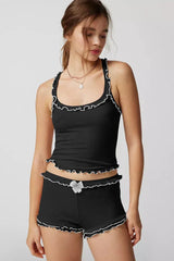 Woman wearing a black ribbed knit tank top and shorts set with ruffle trim and a bow accent.
