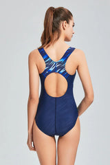Woman in a navy blue one-piece swimsuit, back view showing racerback and cut-out detail