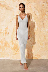 Woman wearing a white knit maxi dress with spaghetti straps and a V-neckline, standing against a textured wall.