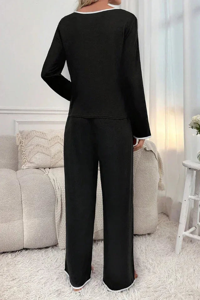 back view of woman wearing black long sleeve pajama set with white piping, standing in a bedroom