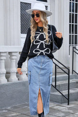woman wearing black crew neck sweater with white bow pattern, blue denim midi skirt, white hat, and sunglasses