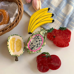 A selection of fruit-shaped hair clips, including bananas, durian, dragon fruit, strawberries, and cherries, alongside a donut and flowers.