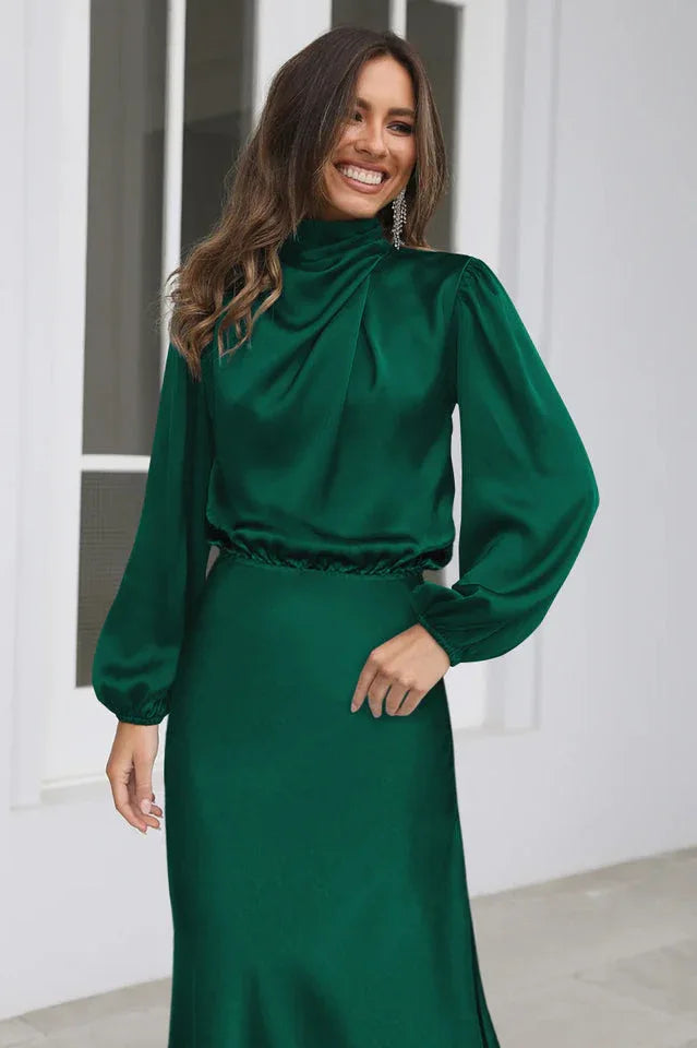 Close-up of a woman wearing an emerald green satin dress with a draped cowl neckline, smiling.