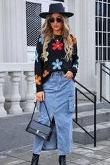 Woman wearing a black long-sleeve sweater with a colorful floral print, denim skirt, black hat, sunglasses, and handbag.