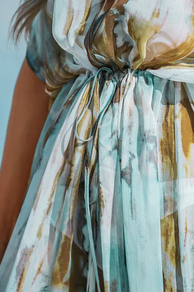 Close-up of the tie-waist detail on a sheer, watercolor print maxi dress.