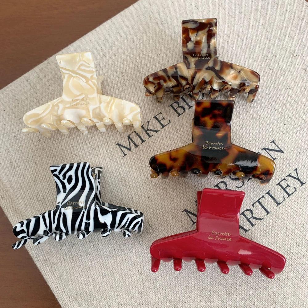 A collection of five hair claw clips in various patterns and colors: tortoiseshell, marbled cream, zebra print, solid red, and a different tortoiseshell.