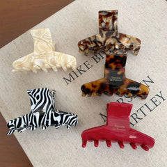 A collection of five hair claw clips in various patterns and colors: tortoiseshell, marbled cream, zebra print, solid red, and a different tortoiseshell.