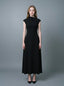 Woman in a black mock neck cap sleeve A-line dress standing against a grey background.