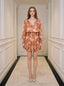 Woman standing in a hallway wearing a floral print mini dress with long sleeves and a V-neck.