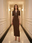 Woman standing in a hallway wearing a brown ribbed knit dress with white trim on the collar and sleeves, and nude high heels.