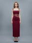 Woman wearing a long, burgundy slip dress with lace waist detailing, standing against a gray background.