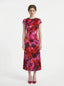 Woman wearing a pink and red floral print satin midi dress with short sleeves and ruched detailing, standing against a white background.