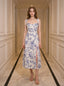 Woman wearing a floral print midi dress with tie shoulder straps and a high slit, standing in a hallway.
