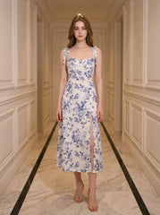 Woman wearing a floral print midi dress with tie shoulder straps and a high slit, standing in a hallway.