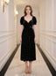 A woman stands in a hallway wearing a black velvet midi dress with a floral print.
