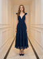 Woman standing in a hallway wearing a navy blue midi dress with ruffle sleeves and a deep V-neckline.