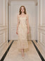 Woman wearing a cream-colored sleeveless midi dress with floral embellishments and a ruffled hem, standing in a hallway.