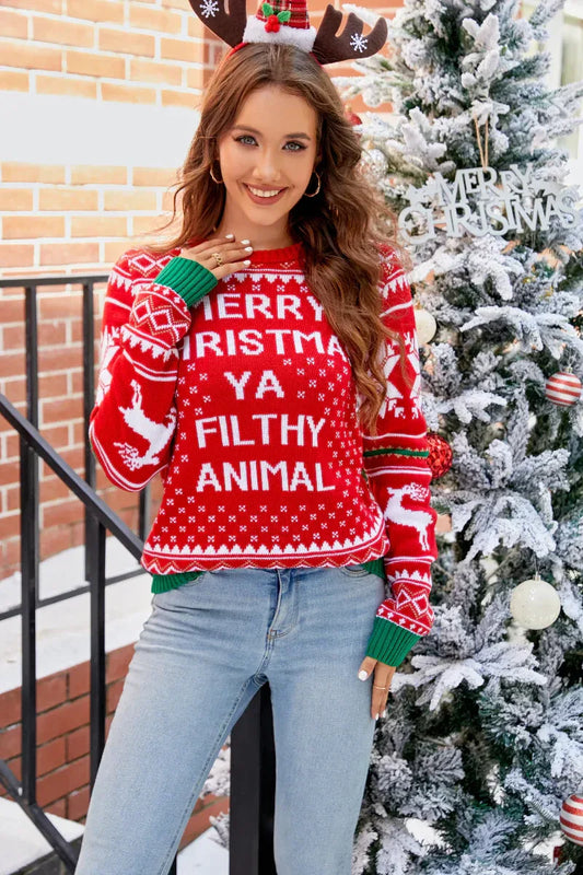 Woman wearing a red Christmas sweater with "Merry Christmas Ya Filthy Animal" text and reindeer graphics, standing next to a decorated Christmas tree.