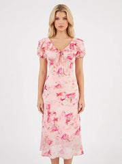 Woman wearing a pink floral print midi dress with short puff sleeves and a tie-front V-neckline, shown from the front.