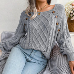 Woman wearing a grey cable knit sweater with buttons, sitting on a couch with a blanket, paired with light wash jeans.